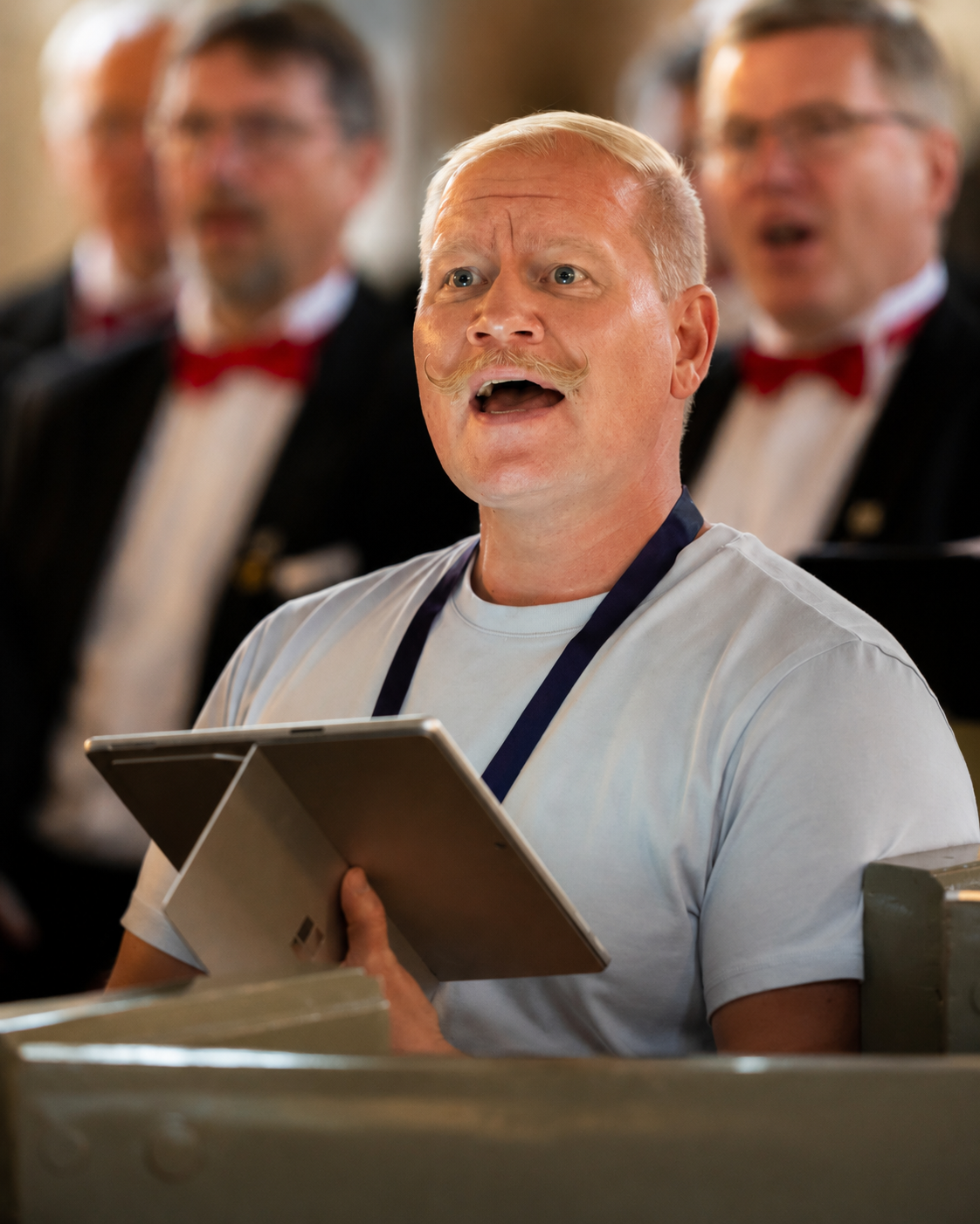 Sebastian Jungar singing with a choir while holding a tablet.